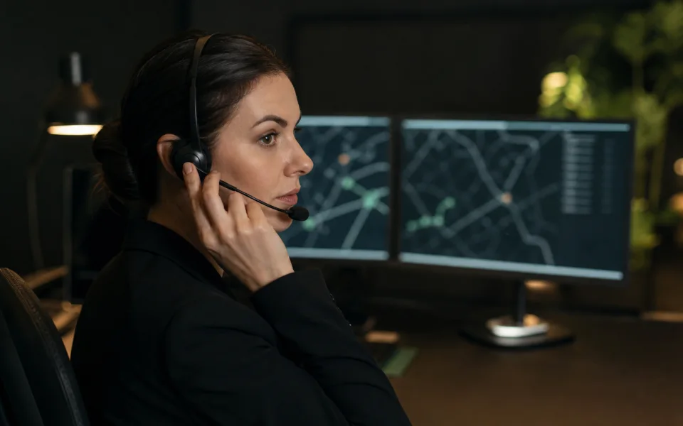 Professional dispatch coordinator handling a call in a dark trip-monitoring workspace.